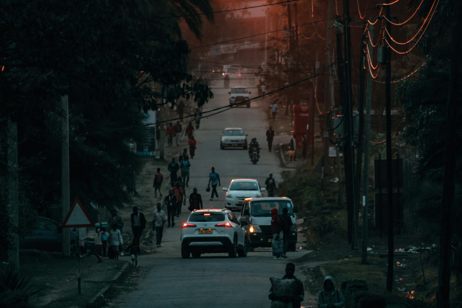 People and cars move down a road at dusk.
